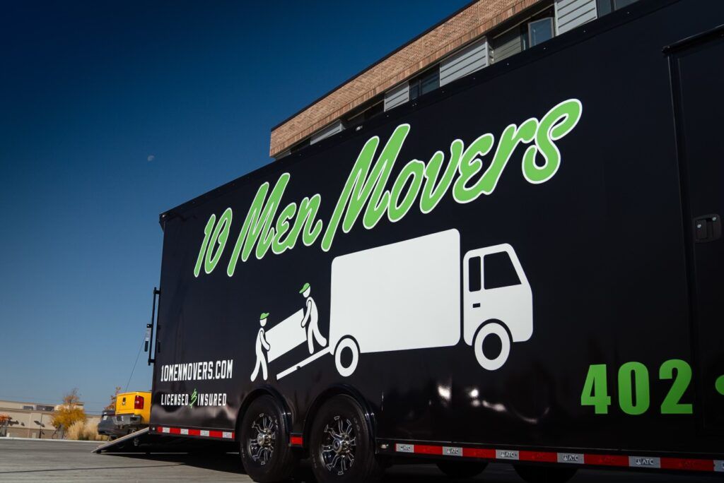 10 Men Movers truck with logo, featuring moving workers and contact information, set against a clear blue sky, emphasizing professional moving services in Omaha.