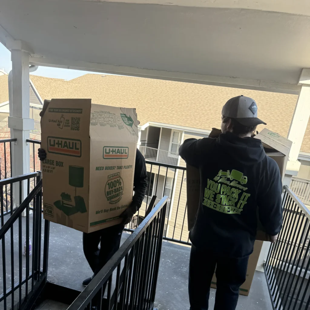 Two movers from 10 Men Movers carrying boxes down an exterior apartment stairwell during an apartment move, handling tight spaces with care and efficiency.