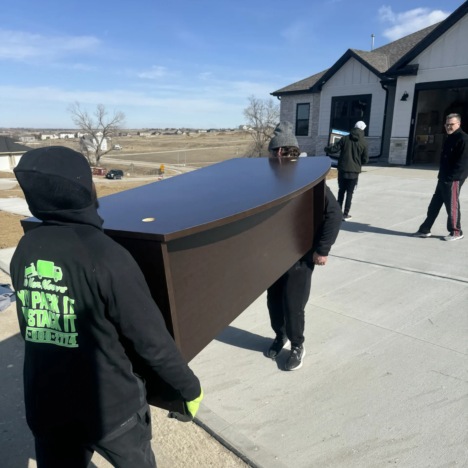 Movers carrying a large brown desk on moving day, showcasing teamwork and preparation for relocation in a suburban setting.