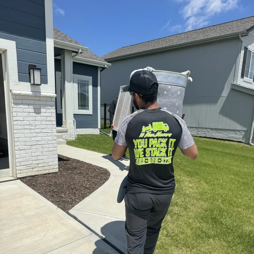 Mover from an Omaha moving company carrying packed items into a suburban home, showcasing efficient, professional service by 10 Men Movers.