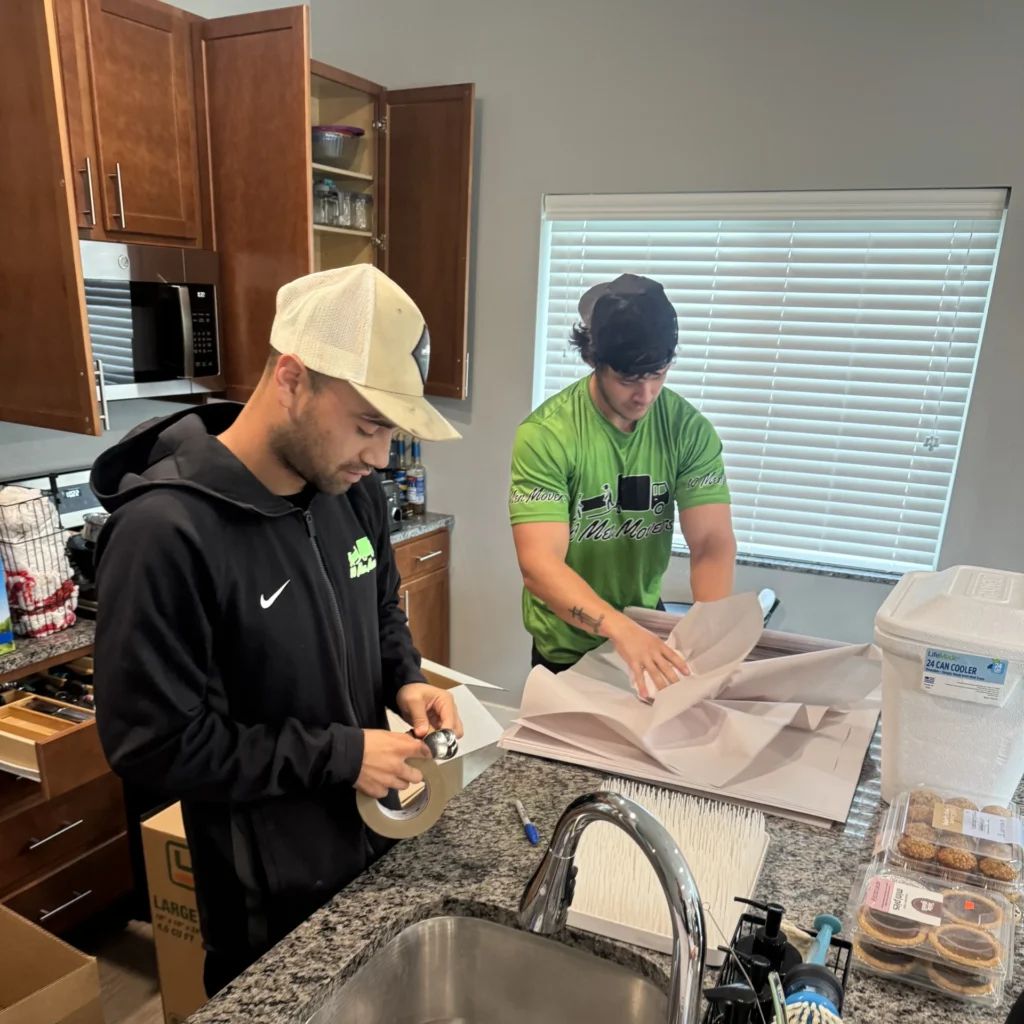 10 Men Movers team acting as professional moving packers, carefully wrapping and packing kitchen items in a modern Omaha home.